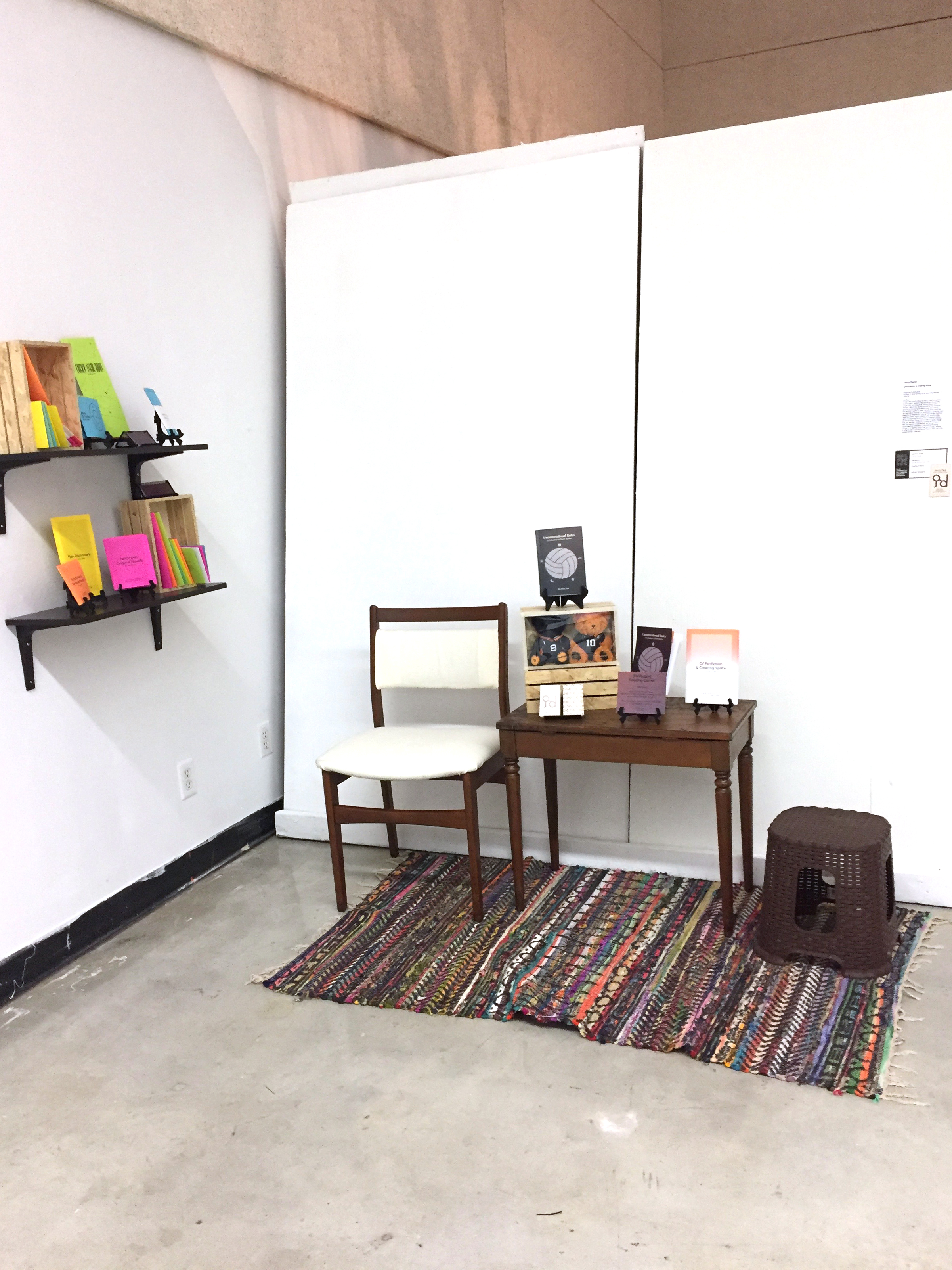 A wide shot capturing the entire Reading Corner. On the left are hanging shelves displaying chapbooks and zines. On the right is the reading space with a table and seats; the table displays several reading materials.